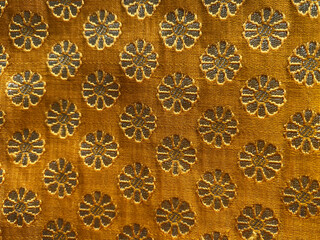 A close-up of luxurious yellow silk fabric adorned with intricate floral brocade weaving.