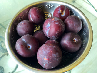 A close-up of ripe plums nestled in a bowl, showcasing their deep purple skin and juicy, vibrant interiors. 