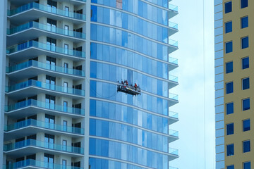 Workers on an outside suspended scaffold platform cleaning a skyscraper building facade with glass windows and balconies .
