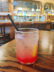 Glass of lemonade with ice and straw on wooden bar table in dimly lit pub.