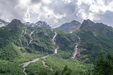 Fototapeta premium Meltwater from the glacier forms waterfalls in the mountains. Glacial water forms waterfalls. Environmentally friendly water flows down from a glacier in the mountains. Landscape with waterfalls.