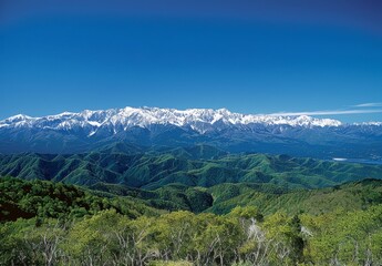 Fototapeta premium mountain range from an angle, clear blue sky, distant snow-capped mountains in background