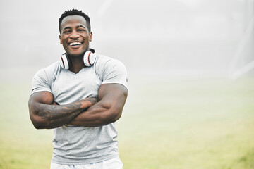 Fototapeta premium Black man, portrait and confidence outdoor for fitness, wellness and health goals achievement in morning. Athlete, face and crossed arms on field for workout, training and exercise with headphones