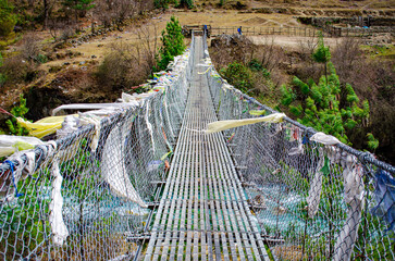 A suspension bridge draped in colorful prayer flags. The prayer flags are a common sight in the...