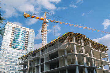A tower construction crane on the background of a blue sky with clouds. The frame of a building under construction. Building construction. Load-bearing reinforced concrete walls of the house.
