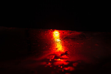 Red light is reflected in the water during the night. The scene is dark and moody. Red light shining through rain on dark surface, creating a moody and atmospheric scene