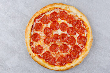 Pepperoni pizza with sausages and cheese mozzarella on a gray concrete countertop. Top view.