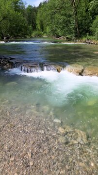 Aerial Drohnenflug in niedriger H&ouml;he &uuml;ber eine Stromschnelle in einem Fluss mit kristallklarem Wasser in den Alpen mit B&auml;umen, Felsen, Hochformat, UHD