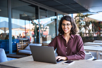 Portrait of 20s latin hispanic freelance business entrepreneur. Smiling businesswoman working remotely online on laptop computer outdoors. Smiling Indian young student woman using pc app for learning