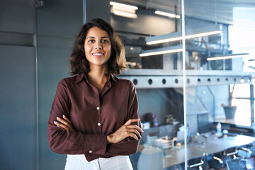 Portrait of beautiful successful hispanic young business woman with crossed arms smiling at camera. Latin or eastern confident middle age female ceo leader businesswoman standing in office. Copy space