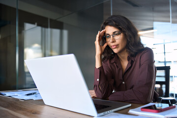 Focused young businesswoman looking at laptop pc computer screen having headache, migraine. Latin...