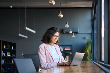 Happy latin hispanic young business woman working on laptop computer in company office. Smiling...