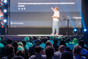 Business professional presenting at a conference with a large audience, highlighting key points on...