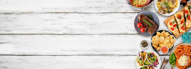 Side border of various delicious foods. Top down view on a white wood banner background. Copy space. Pastas, flatbreads, tacos, steak and restaurant theme dishes.