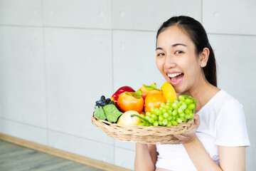 Young smiling woman posing with basket of fresh vegetables. Time of healthy food, bananas, apple, tomato, green grapes. Vegetables and Fruits.