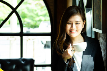 Charming young woman keeping cup of hot drink after online meeting. Young woman enjoying hot coffee in the morning in coffee shop. Work from Home concept.