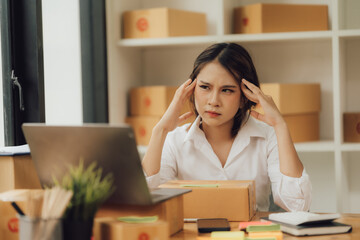 Young Asian woman sits at home and checks laptop computer orders from boxes of various sizes. Ideas for starting a business