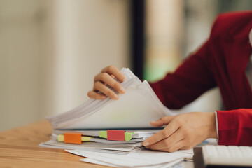 The businesswoman's hands are busy working amidst stacks of paper files, searching and checking for...