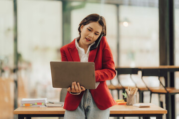 Busy Businesswoman on a Call: A determined young businesswoman multitasks, skillfully handling a laptop and a phone call in a modern, bright office setting.  The image conveys efficiency, ambition.