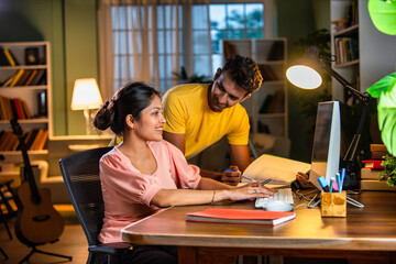 Indian Asian young woman and man studying together at home on a computer, focused on online learning
