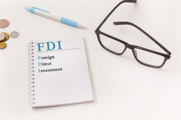 The Foreign Direct Investment concept with letters FDI written on notebook and business office items like pen, coins, and glasses