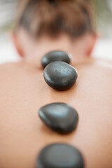 Spa, calm and woman with rocks for massage, luxury treatment or stress relief on bed. Rear view,...