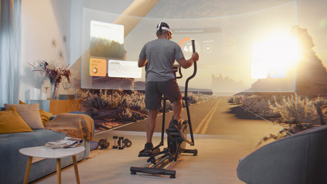 African American sportsman wearing AR headset trains on orbitrek. Virtual screen shows landscape and fitness application interface with timer and health care statistics. Metaverse futuristic home gym.