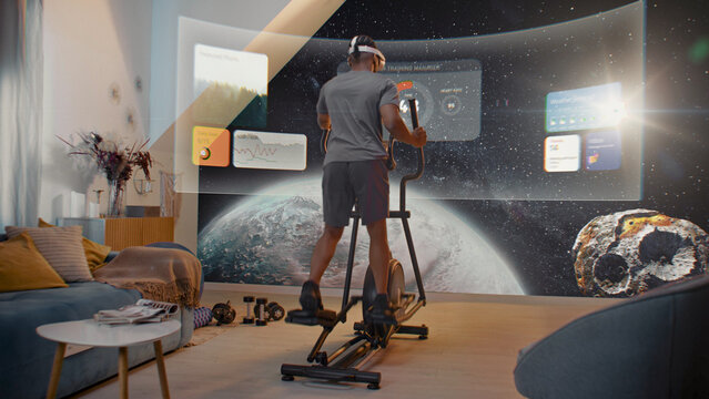 Metaverse futuristic home gym. African American athlete in VR headset training on orbitrek. Virtual screen shows image of the universe and AR workout app with icons, timer and health care statistics.