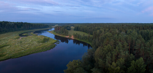 A river with a forest on either side. The water is calm and the sky is a mix of blue and purple