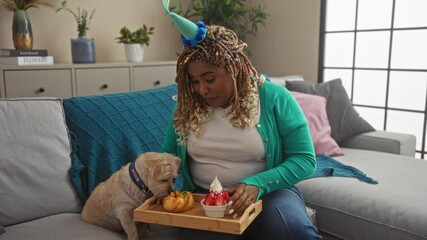 A joyful woman in a bright living room shares a celebratory snack with her dog from a wooden tray on the couch.
