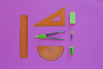 green set of geometry tools with compass, rulers, eraser and sharpener lie on a pink background,...