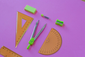 set of green geometry tools: rulers, compasses, eraser and sharpener lie on a pink background