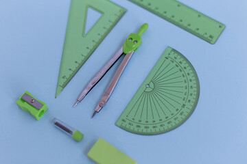 set of green geometry tools: rulers, compasses, eraser and sharpener lie on a blue background. Mathematics and lesson at school