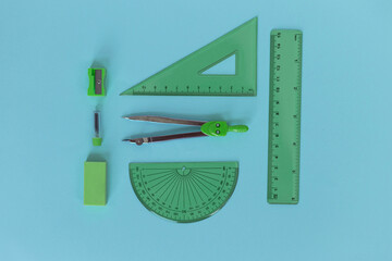 set of green geometry tools: rulers, compasses, eraser and sharpener lie on a blue background.