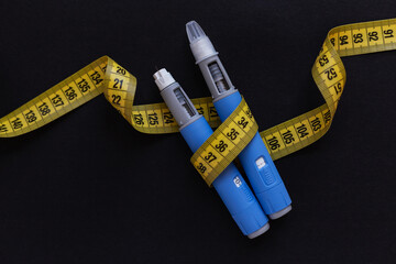 Two drugs injection pens ozempic for weight loss with a measuring yellow tape on a black...