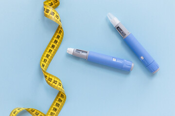 Two drugs injection ozempic for weight loss with a measuring yellow tape on a blue background. Drug...