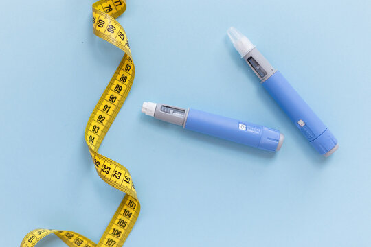 Two drugs injection ozempic for weight loss with a measuring yellow tape on a blue background. Drug pen for diabetics and weight loss, top view. antidiabetic medication or anti-obesity medication