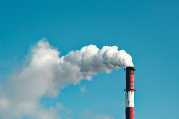Industrial smoke stack releasing dense white smoke into the clear blue sky