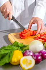A person in a white shirt is chopping vegetables on a wooden cutting board in the kitchen