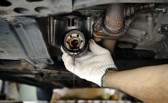 A mechanic is holding a used oil filter and removing it from a car. Male hand is changing the oil filter for maintenance.