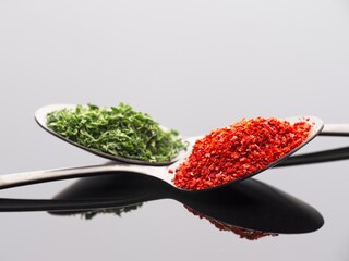 Pepper and parsley flakes on reflective surface.