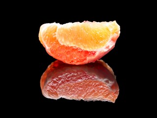 Grapefruit wedge on black reflective surface.