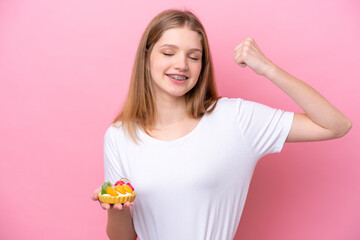 Teenager Russian girl holding a tartlet isolated on pink background doing strong gesture