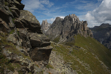 A hiking trail above the tree line in the Stubai Alps with a lightly cloudy sky and towering gray mountains in the background.