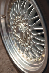 a shiny disc, cast in one piece from a light alloy of metals, a wheel of a car of old times. Close up of vehicle details. Concept of style and racing. Selective focus. Vertical photo