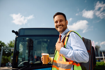 Happy bus driver with takeaway coffee coming to work at looking at camera.