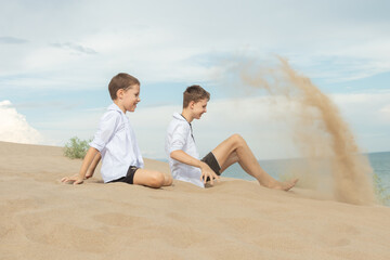 Fototapeta premium Two Boys Playing with Sand on Beach: Childhood Adventure and Time Metaphor by Ocean Shore