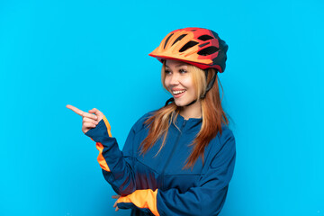 Young cyclist girl isolated on blue background pointing finger to the side and presenting a product