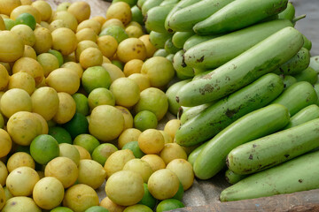 Fresh green bottle gourds and yellow lemons for sale displayed on wooden table at outdoor farmers market