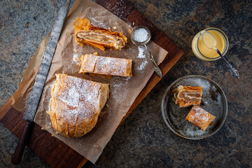 Traditional Bavarian apfelstrudel with backed apples, raisins and icing sugar served as top view on a wooden design board with backing paper